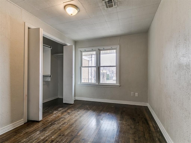 unfurnished bedroom with visible vents, dark wood-type flooring, a closet, baseboards, and a textured wall