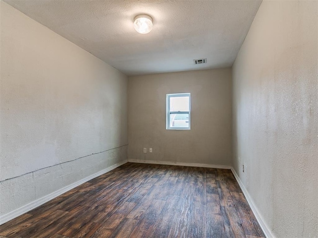 empty room with visible vents, a textured ceiling, wood finished floors, and a textured wall