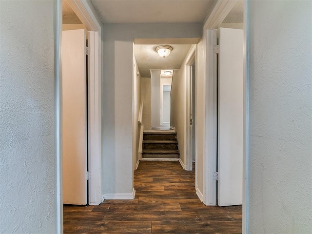 corridor with wood finished floors, baseboards, and a textured wall