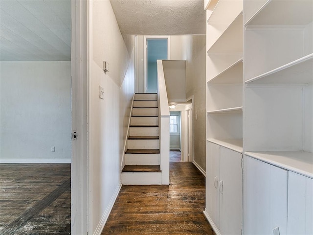 staircase featuring baseboards, wood-type flooring, and a textured ceiling