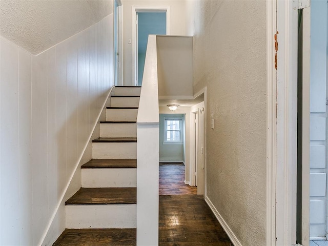 stairway with a textured ceiling, a textured wall, and hardwood / wood-style flooring