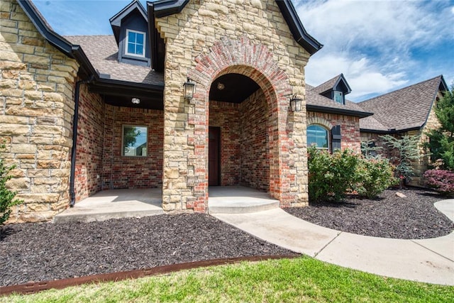 doorway to property with brick siding, stone siding, and roof with shingles