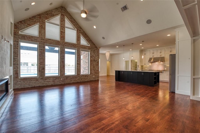 unfurnished living room with visible vents, high vaulted ceiling, a sink, ceiling fan, and dark wood-style flooring