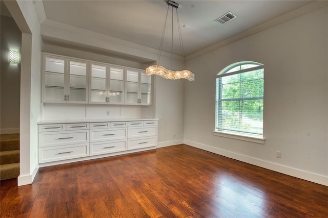 unfurnished dining area featuring dark wood-type flooring, crown molding, visible vents, and baseboards