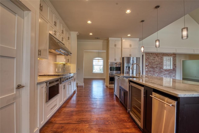 kitchen with pendant lighting, under cabinet range hood, appliances with stainless steel finishes, white cabinets, and dark wood-style flooring