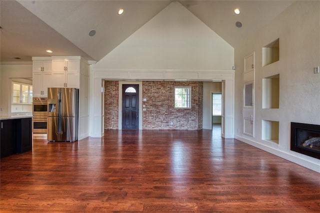 unfurnished living room featuring visible vents, brick wall, dark wood-type flooring, a glass covered fireplace, and high vaulted ceiling