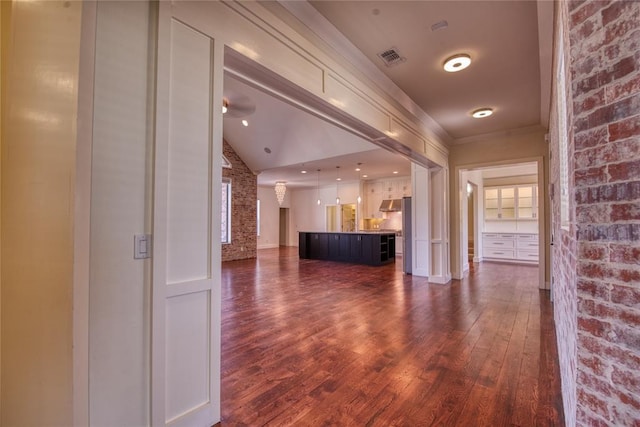 hall featuring visible vents, ornamental molding, dark wood finished floors, brick wall, and lofted ceiling