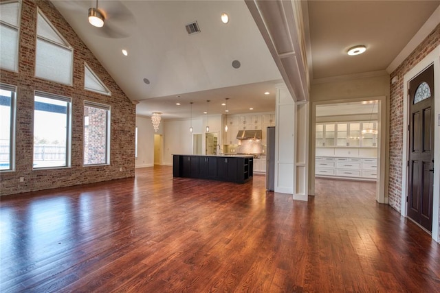 unfurnished living room featuring visible vents, high vaulted ceiling, brick wall, ceiling fan, and dark wood-style flooring