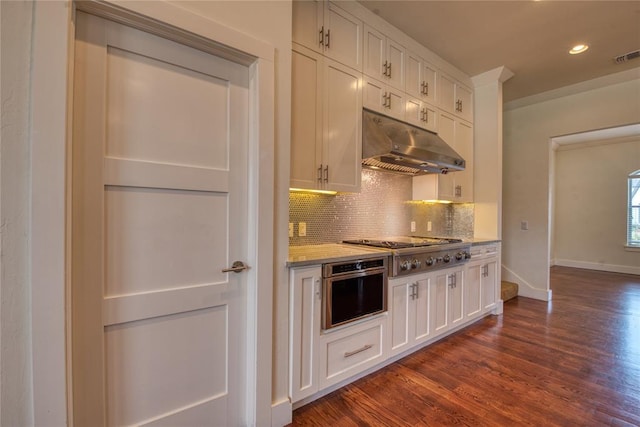 kitchen with backsplash, under cabinet range hood, dark wood finished floors, appliances with stainless steel finishes, and white cabinets