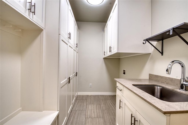 kitchen featuring light stone countertops, white cabinetry, baseboards, and a sink