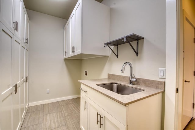 kitchen featuring light wood-type flooring, a sink, white cabinets, light countertops, and baseboards