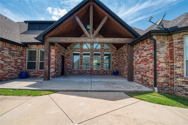 view of exterior entry featuring brick siding and a shingled roof