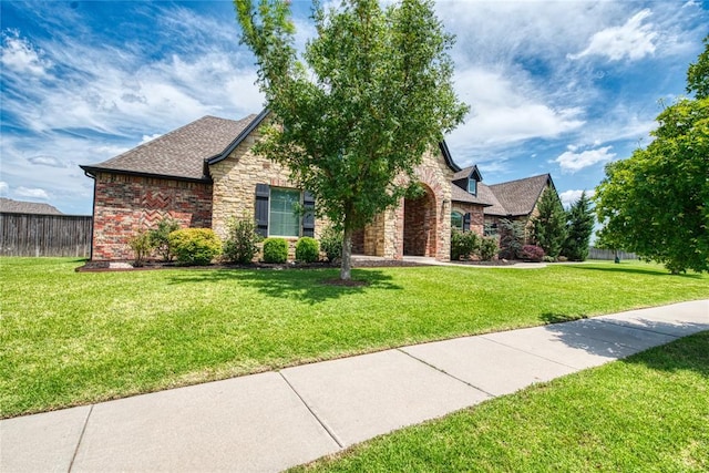 view of front of home with stone siding, a shingled roof, a front lawn, and fence