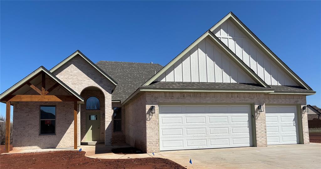 view of front of property with driveway, roof with shingles, board and batten siding, a garage, and brick siding