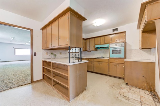 4801 Del Crest Dr, Del City, OK 73115 - kitchen with oven, under cabinet range hood, light countertops, decorative backsplash, and brown cabinetry