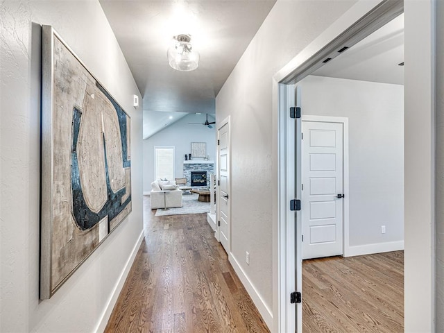 hallway with lofted ceiling, baseboards, and wood finished floors