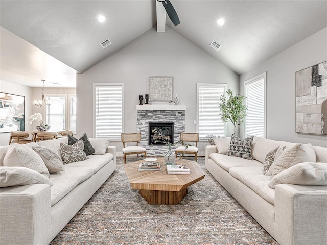 living area with visible vents, beamed ceiling, high vaulted ceiling, ceiling fan with notable chandelier, and a fireplace