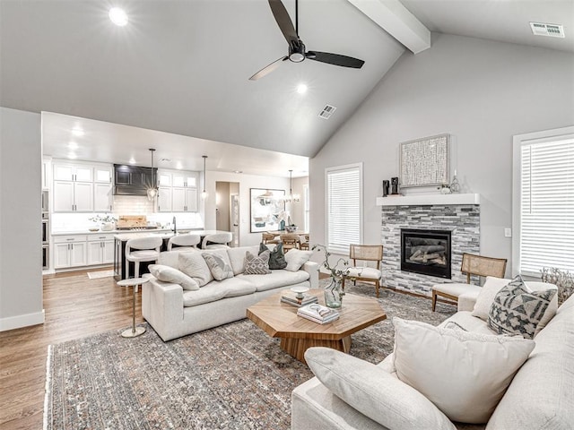 living area featuring visible vents, beamed ceiling, a ceiling fan, and light wood finished floors