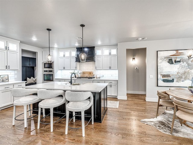 kitchen with light countertops, custom range hood, an island with sink, and light wood-type flooring