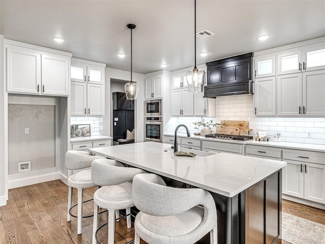 kitchen with glass insert cabinets, light countertops, custom range hood, light wood-style floors, and stainless steel appliances