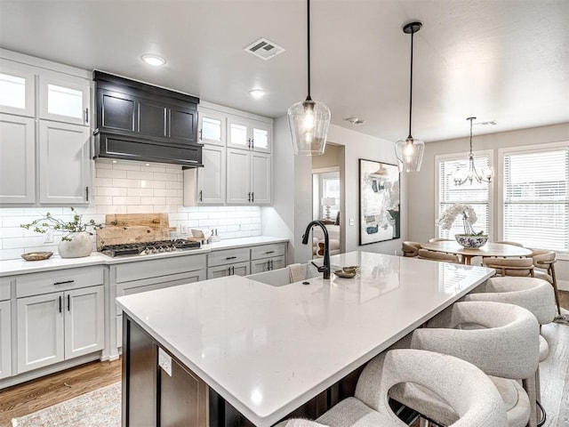 kitchen with visible vents, premium range hood, light wood-style flooring, a sink, and decorative backsplash