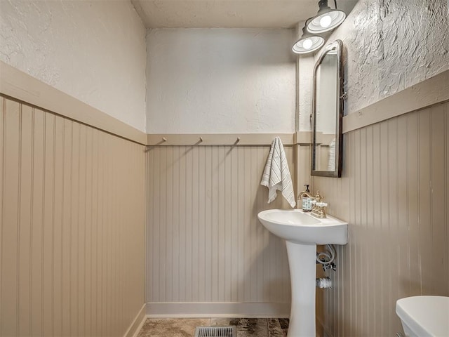 bathroom featuring visible vents, toilet, wooden walls, and a textured wall