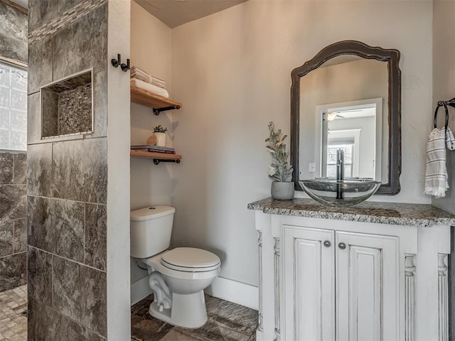 bathroom featuring baseboards, toilet, vanity, and a walk in shower