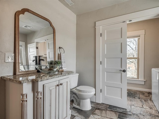 bathroom featuring stone tile flooring, visible vents, toilet, and vanity