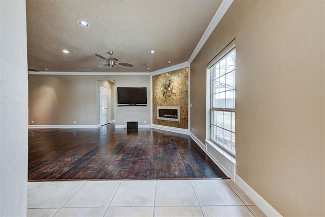 unfurnished living room with baseboards, ceiling fan, crown molding, and tile patterned flooring