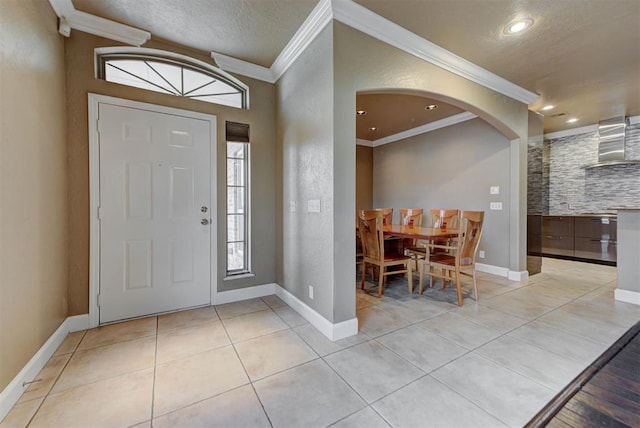 foyer entrance featuring light tile patterned floors, baseboards, arched walkways, a textured ceiling, and crown molding