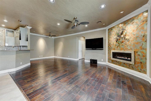 unfurnished living room featuring wood finished floors, a ceiling fan, visible vents, baseboards, and a glass covered fireplace