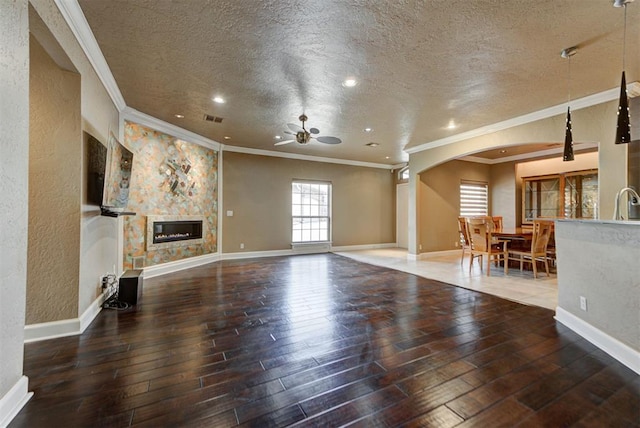 unfurnished living room with visible vents, a textured ceiling, arched walkways, wood-type flooring, and ceiling fan