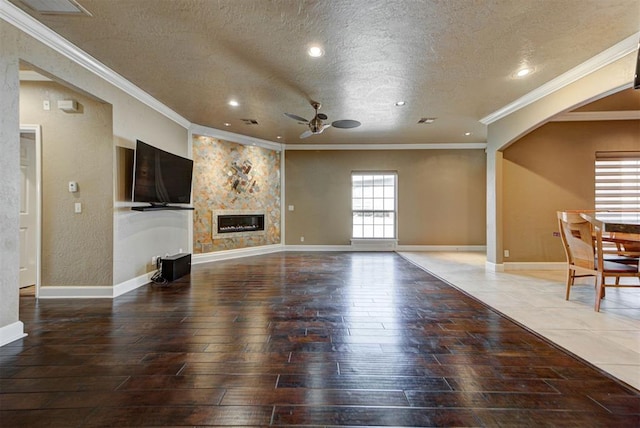 unfurnished living room featuring a textured ceiling, wood finished floors, arched walkways, baseboards, and ceiling fan