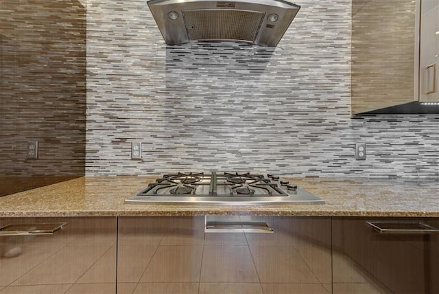 kitchen with decorative backsplash, exhaust hood, light stone countertops, and stainless steel gas cooktop