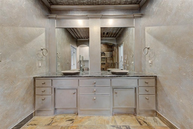 bathroom with double vanity, stone tile floors, a textured wall, and ornamental molding