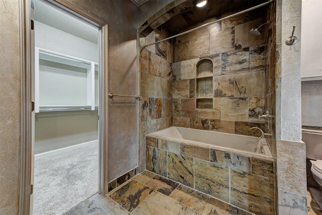 bathroom with stone tile flooring, toilet, and tiled shower / bath