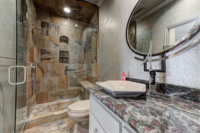 bathroom with vanity, stone tile floors, a shower stall, toilet, and a textured wall