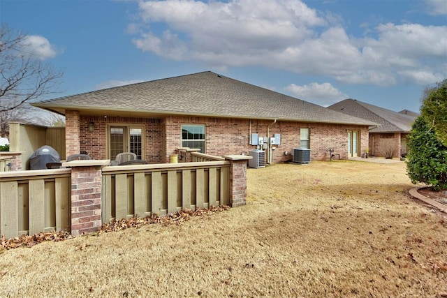 rear view of house with roof with shingles, central AC unit, and brick siding