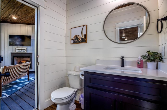 half bath with vanity, wood finished floors, a lit fireplace, wooden ceiling, and toilet