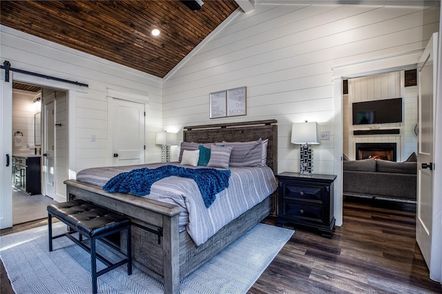 bedroom featuring dark wood-style floors, high vaulted ceiling, a warm lit fireplace, wood ceiling, and a barn door