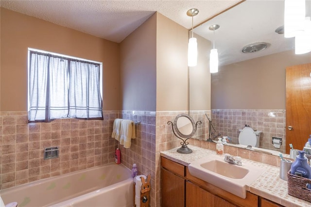 bathroom featuring a garden tub, a textured ceiling, tile walls, wainscoting, and vanity