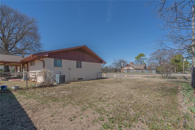 view of side of property featuring fence, a yard, central AC, board and batten siding, and brick siding