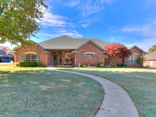 ranch-style home featuring brick siding, a front lawn, and roof with shingles