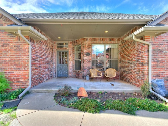 view of exterior entry with brick siding and roof with shingles