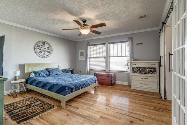 bedroom with crown molding, a barn door, visible vents, and light wood-type flooring