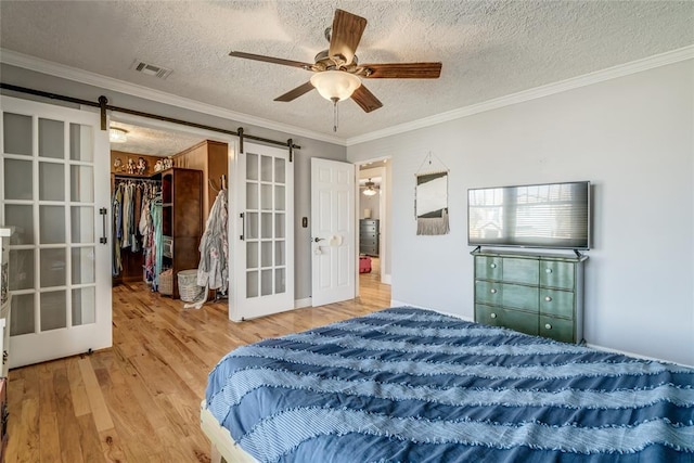 bedroom featuring a barn door, ornamental molding, visible vents, and light wood-type flooring