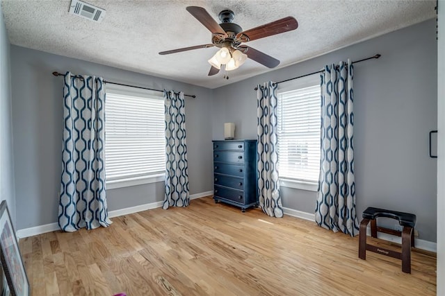 bedroom with a textured ceiling, wood finished floors, visible vents, and baseboards