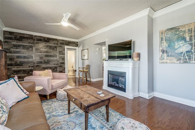 living room with baseboards, ceiling fan, ornamental molding, wood finished floors, and a glass covered fireplace