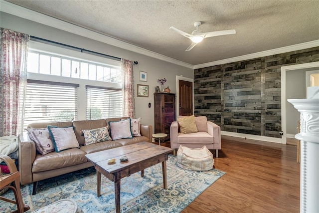 living room featuring wood finished floors, baseboards, ceiling fan, a textured ceiling, and crown molding