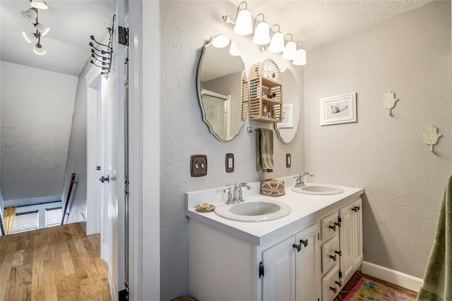 bathroom featuring a textured ceiling, wood finished floors, a textured wall, and a sink